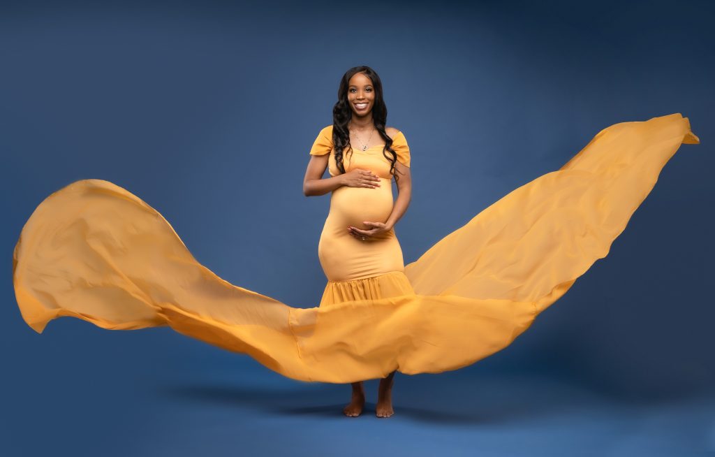 Black pregnant woman in yellow maternity dress and holding her belly