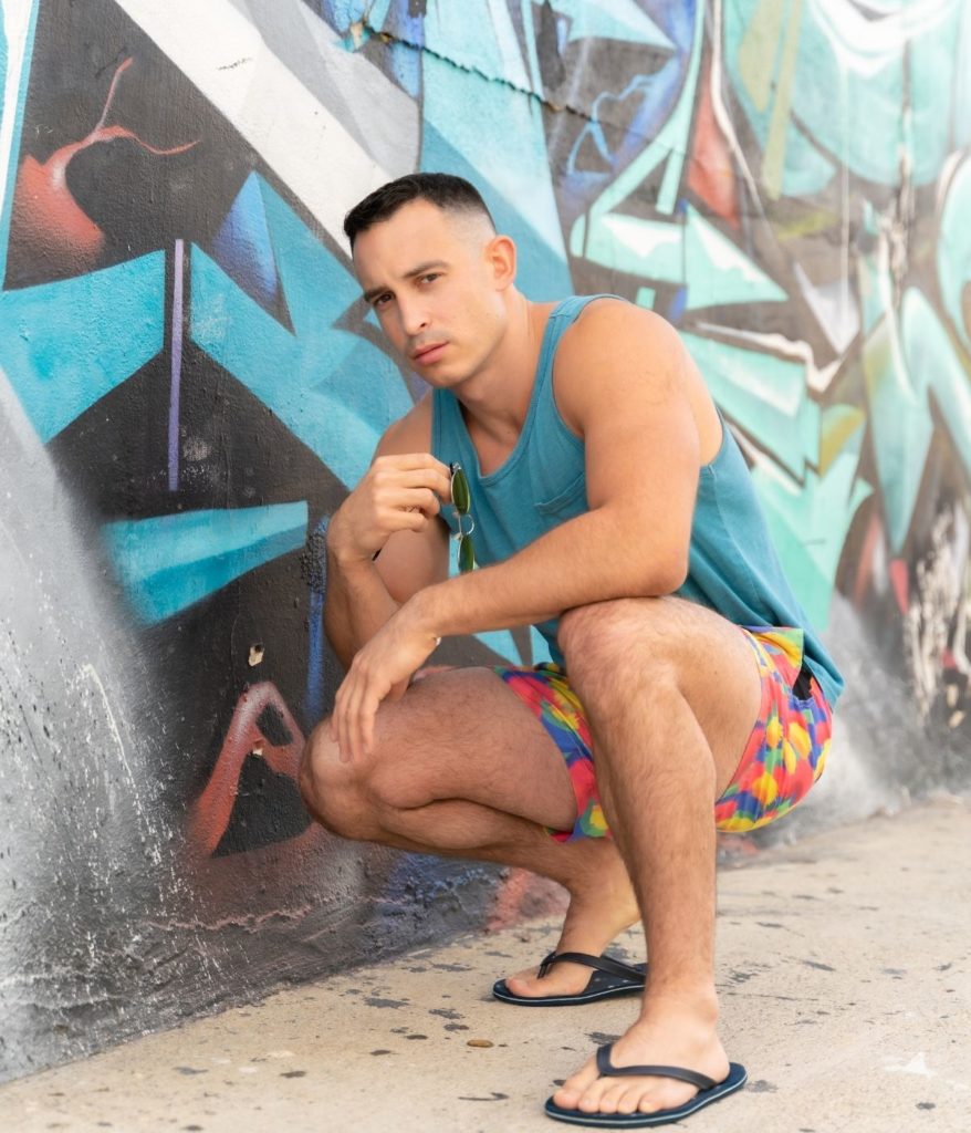 Male model posing for North Park photoshoot in tank top, shorts, and flip flops.